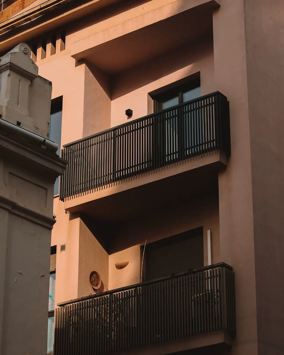 Balkon s tamnom metalnom ogradom od uspravnih šipki na fasadi kuće